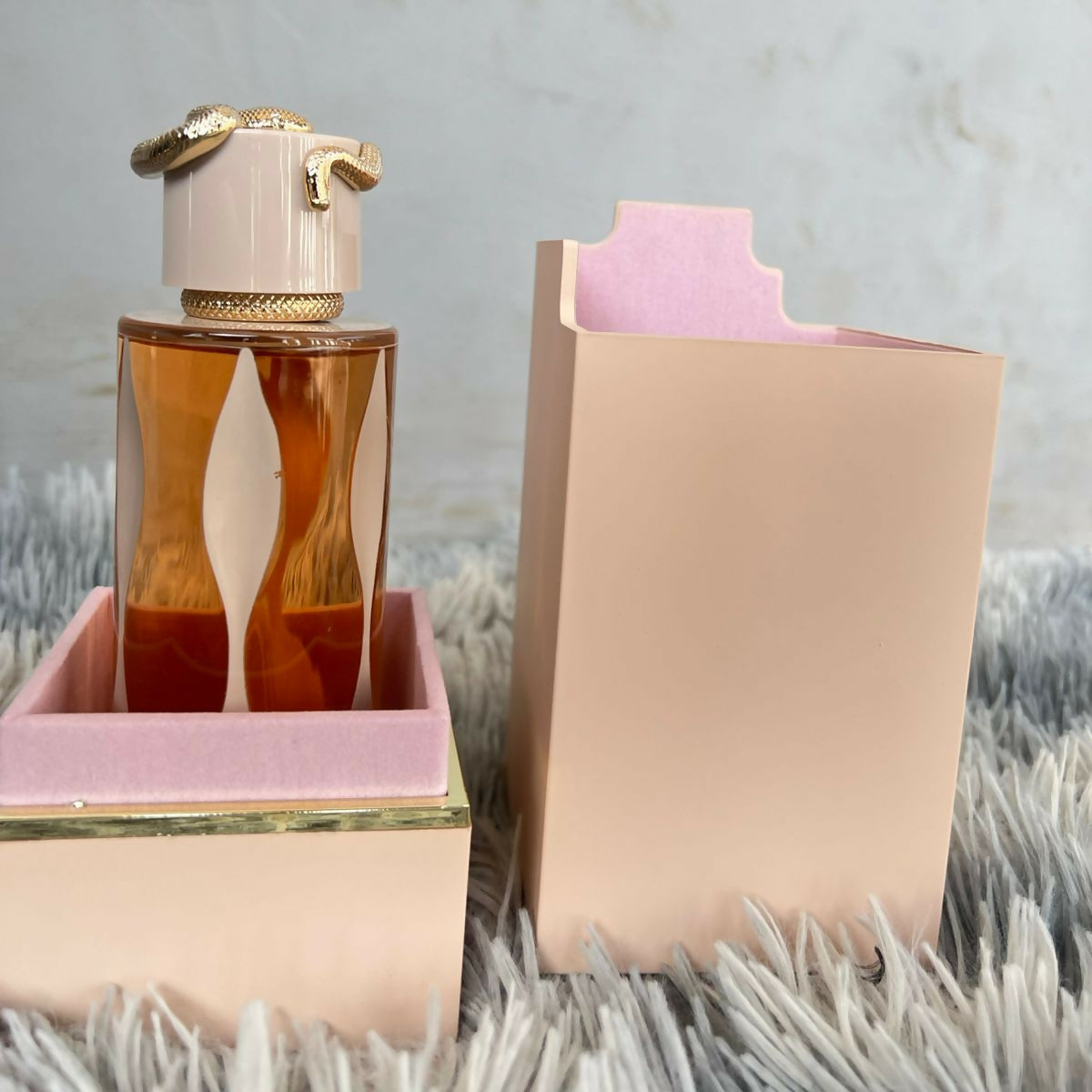 Perfume bottle with gold cap and pink packaging on a textured surface