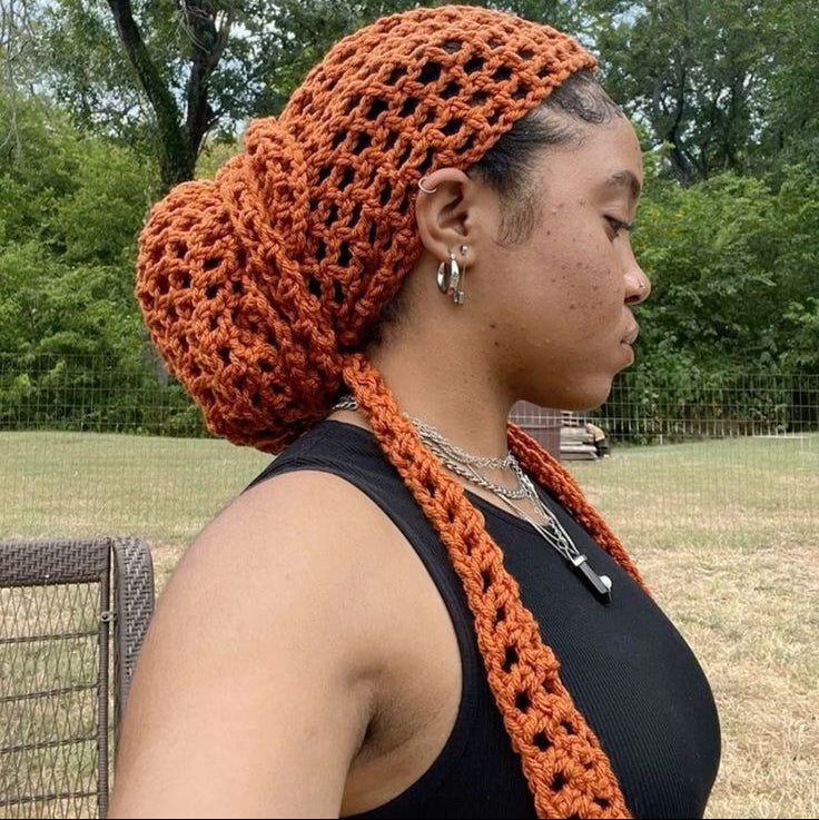 Woman wearing an orange knitted headscarf and matching scarf outdoors with trees in the background