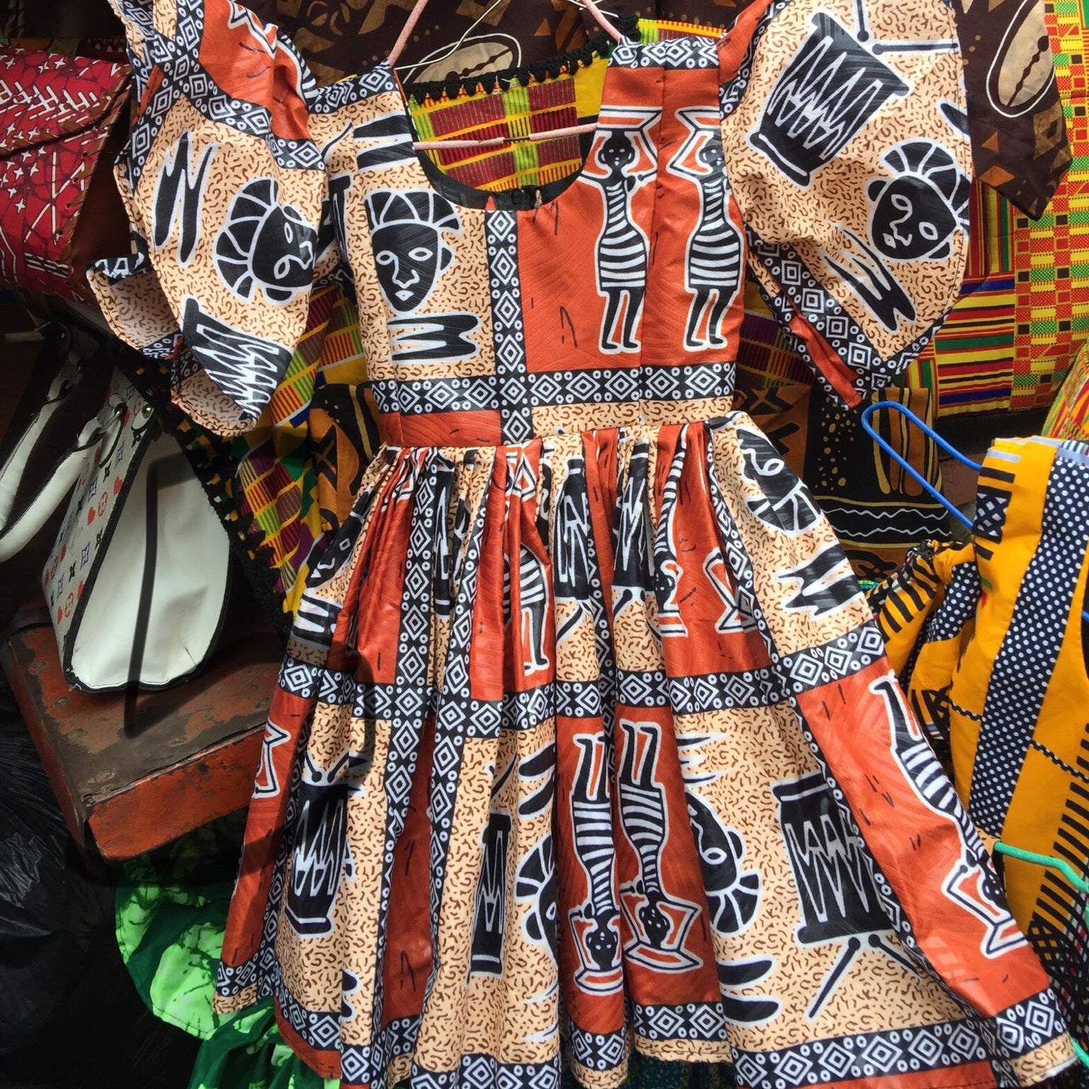 Traditional African dress with intricate patterns and colors, displayed against a colorful background.