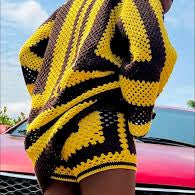 Person wearing a yellow and black patterned crochet sweater with a blue sky background