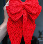 Red crocheted bow held by a hand against a blurred background
