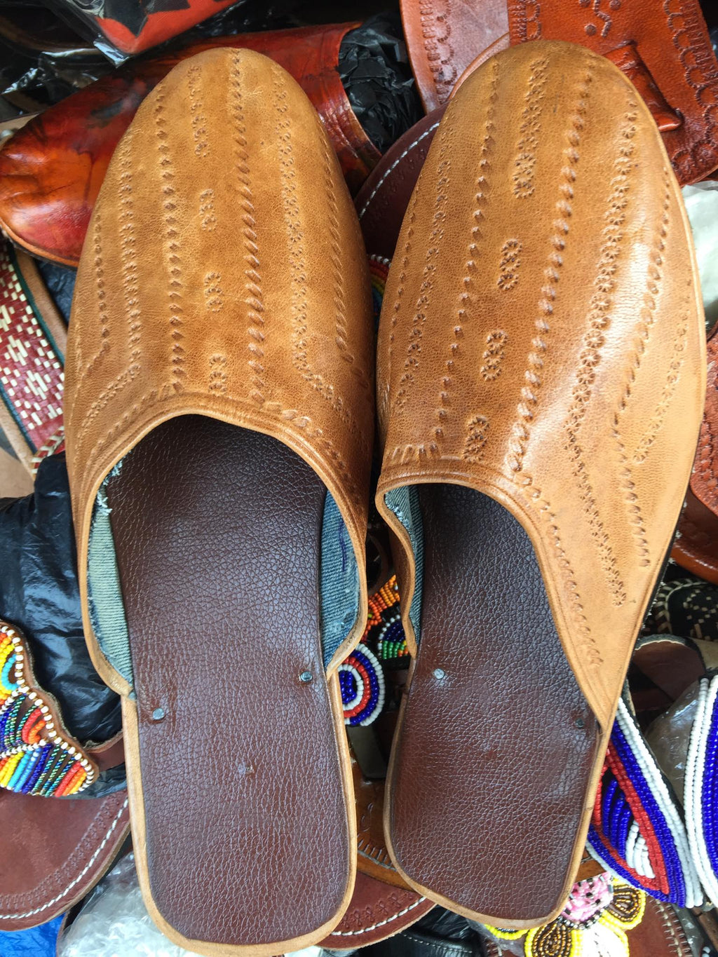 Pair of brown leather slippers with a detailed pattern on a colorful background