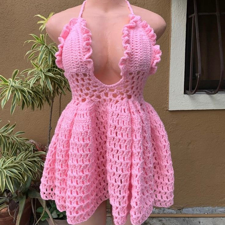 Pink crochet dress on a mannequin against a beige wall with plants.