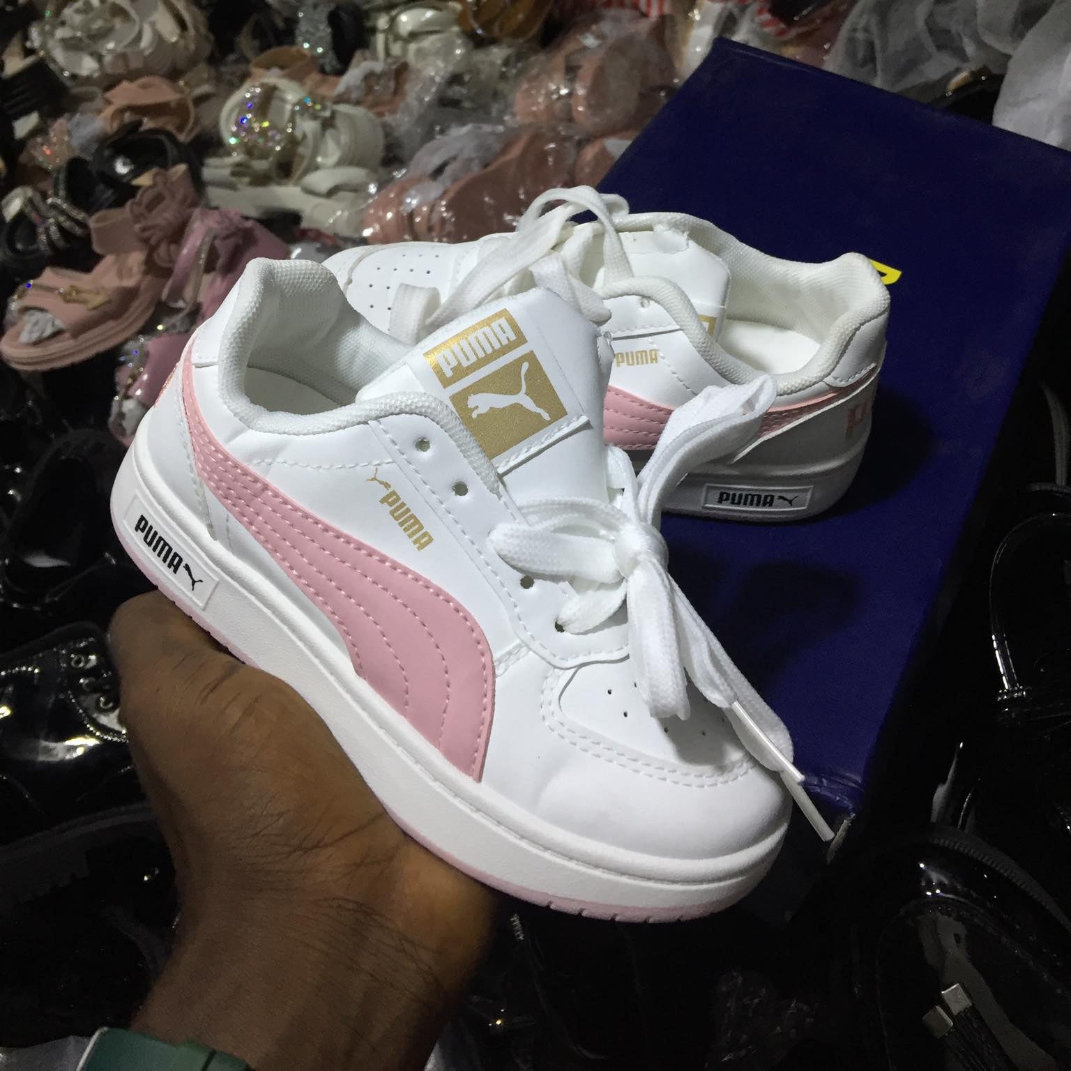 White and pink Puma sneaker held in a hand with a cluttered background