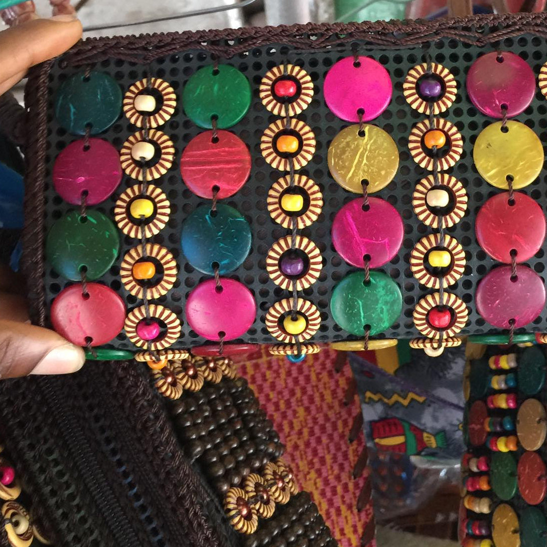 Colorful embroidered fabric with bead patterns held by a hand against a blurred background