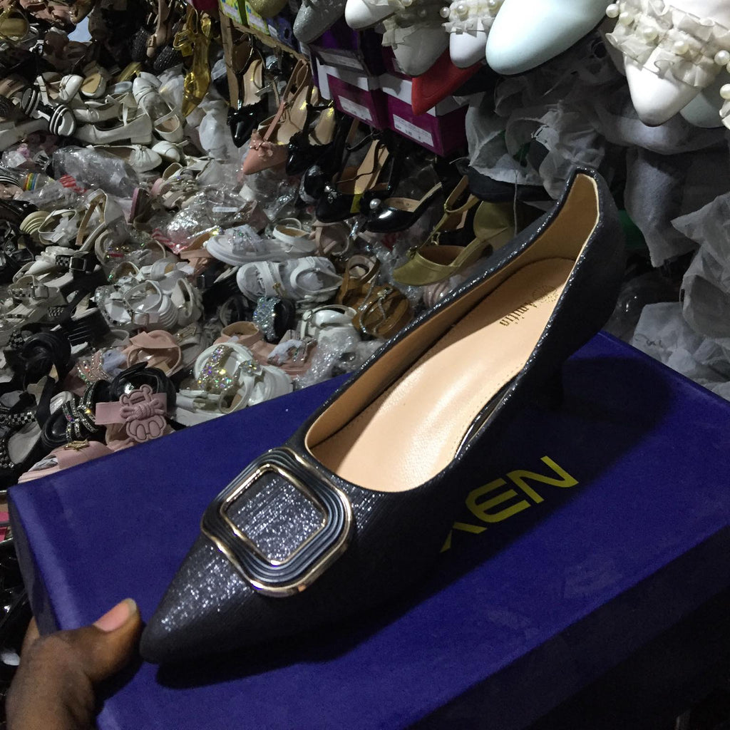 Black glittery shoe with gold buckle on a blue box, surrounded by other shoes.