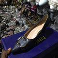 Black glittery shoe with gold buckle on a blue box, surrounded by other shoes.