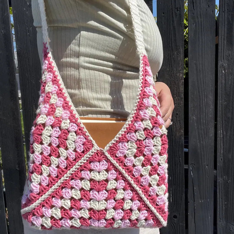 Person holding a pink and white crocheted bag against a wooden fence background