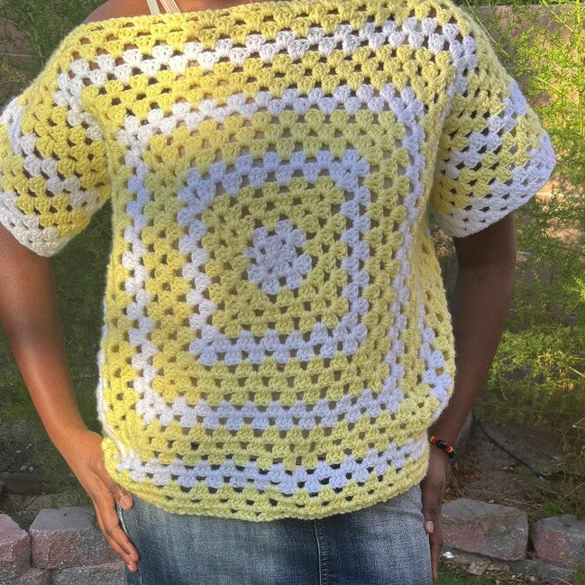 Person wearing a yellow and white crocheted square pattern top outdoors.