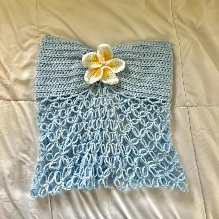 Blue knitted pouch with a yellow flower on a beige surface
