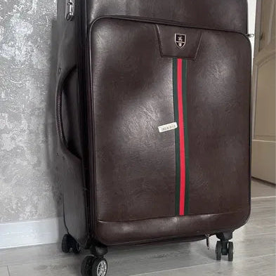 Brown suitcase with a red stripe on a gray floor against a textured wall.