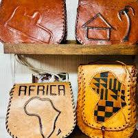 Collection of leather bags with African designs on a wooden shelf.