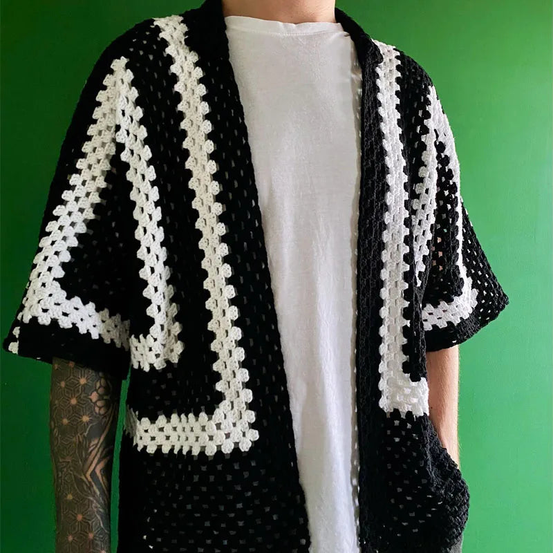 Person wearing a black and white crocheted cardigan against a green background