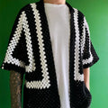Person wearing a black and white crocheted cardigan against a green background