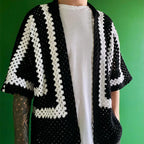 Person wearing a black and white crocheted cardigan against a green background