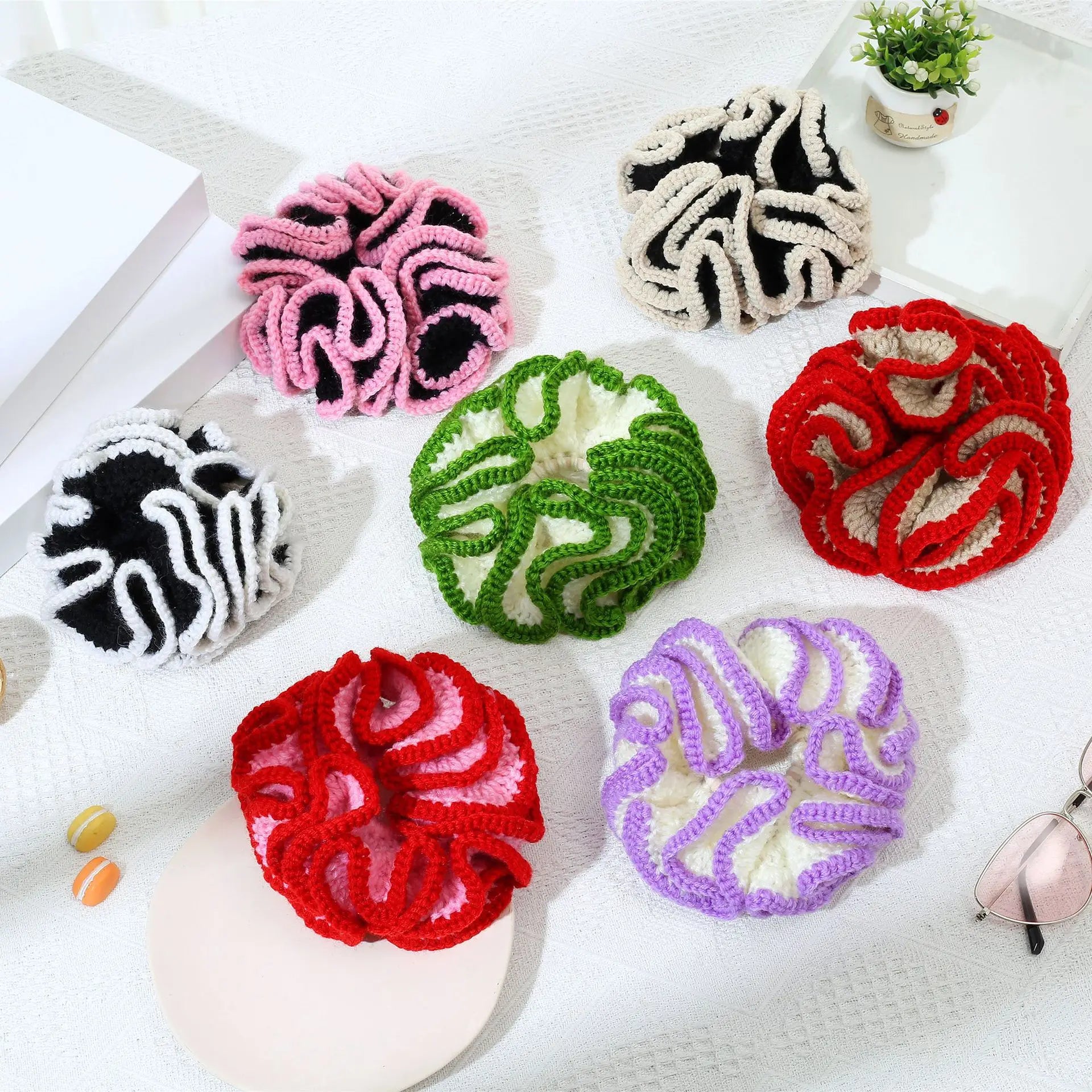 Colorful crocheted coasters on a white surface with a plant and sunglasses in the background.