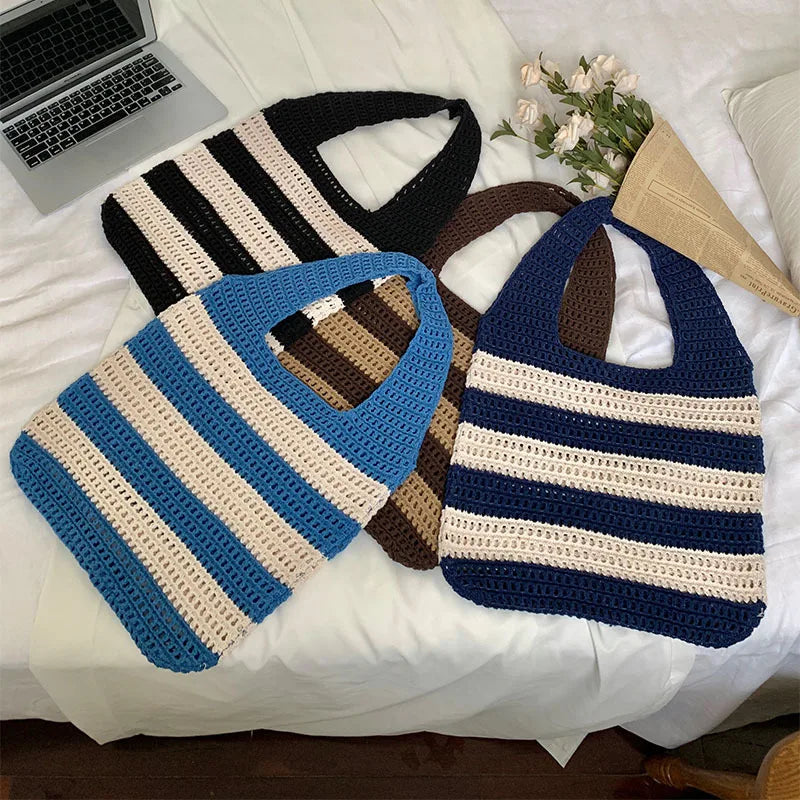 Three striped crochet bags on a white surface with a laptop and flowers in the background.
