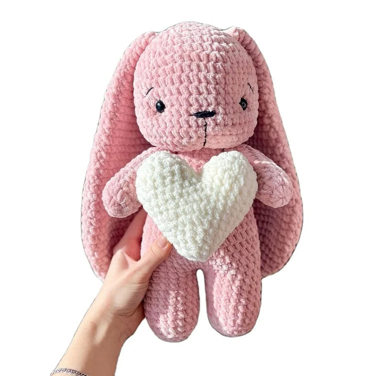 Pink plush bunny holding a white heart, against a white background