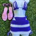 Mannequin wearing a purple and white striped bikini with matching skirt, pink sandals, and sunglasses on grass.