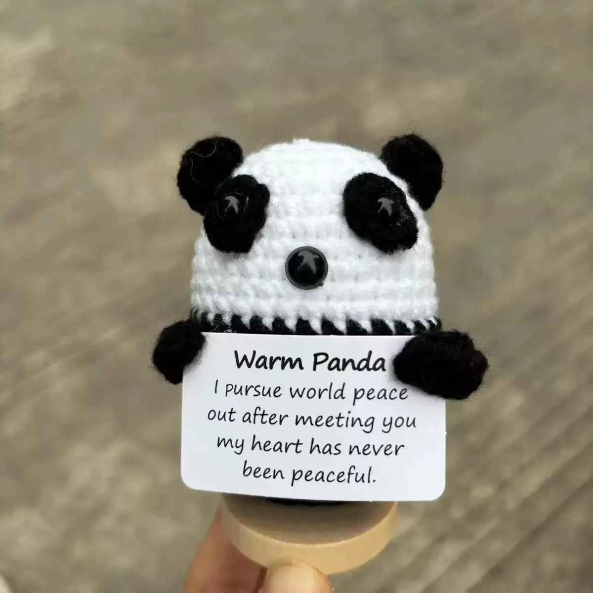 Crocheted panda holding a card with text on a blurred background