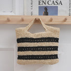 Woven bag with black and beige stripes hanging on a wooden rack.