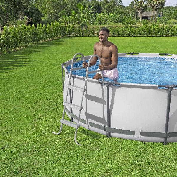 Man standing by a above-ground pool in a grassy area with trees in the background