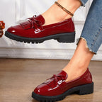 Red loafers with tassels worn by a person on a wooden floor.