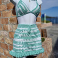 Green and white crochet bikini set on a mannequin against a brick wall.