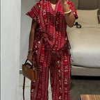 Person wearing a red patterned outfit taking a mirror selfie in a bedroom.