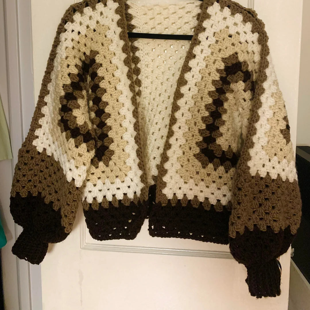 Brown and beige knitted sweater on a hanger against a white wall