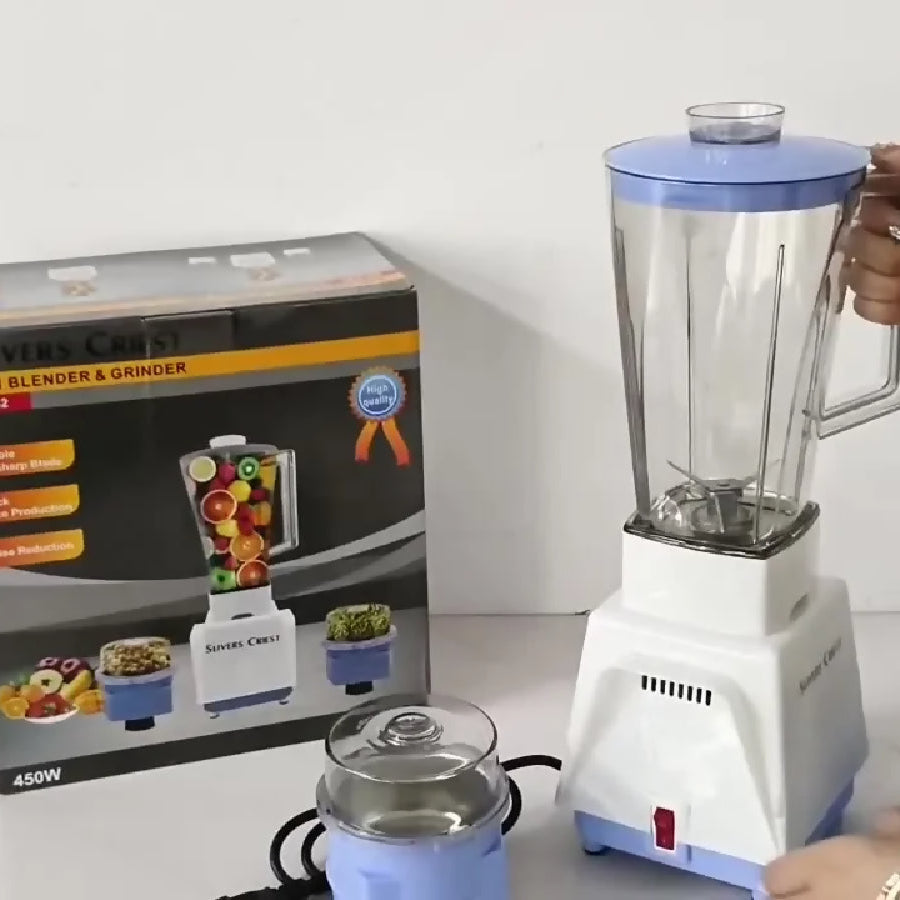Blender with a hand holding its handle, next to a box and additional containers on a white surface.