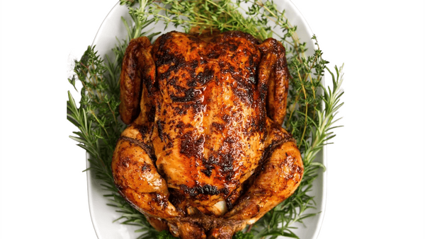 Roasted chicken on a bed of herbs on a white plate. whole roasted chicken from Town Bakery
